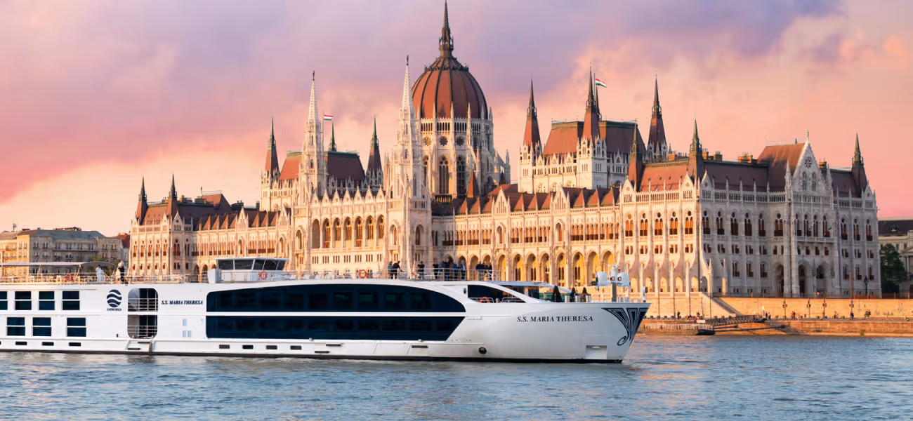 White river cruise ship S.S. Maria Theresa on the Danube in front of the Hungarian Parliament building at sunset.